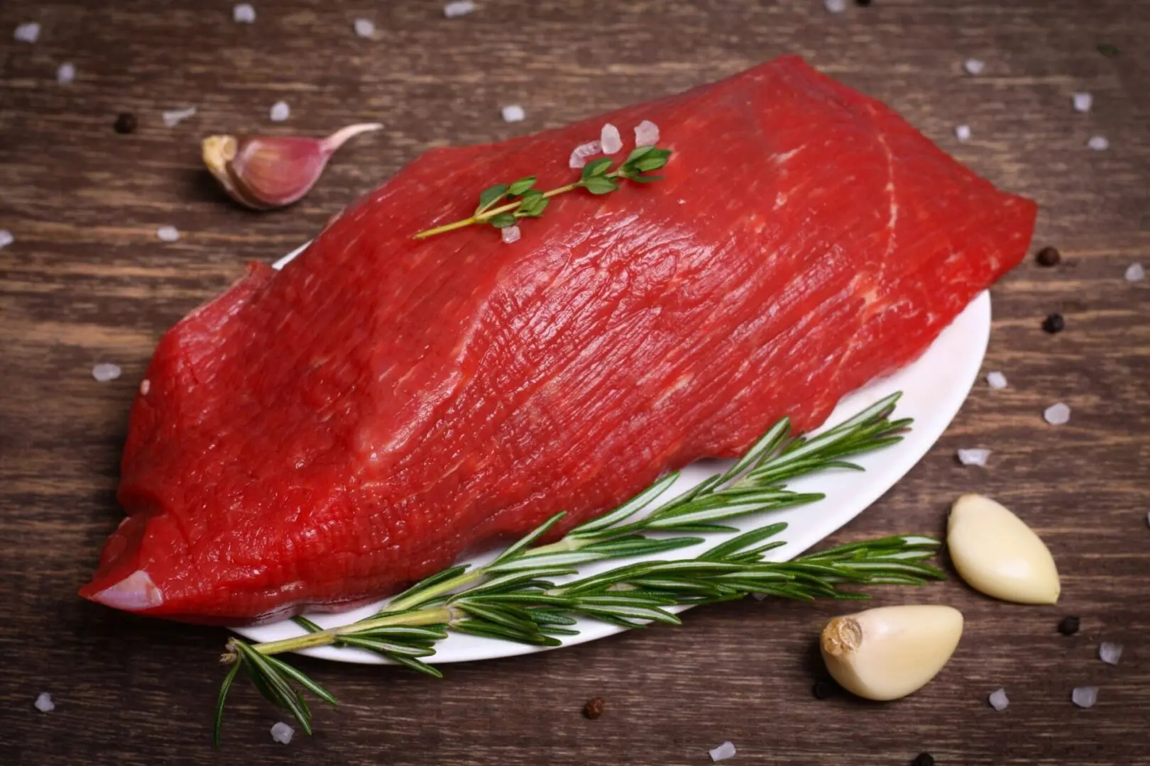 A piece of meat on a plate with garlic and rosemary.