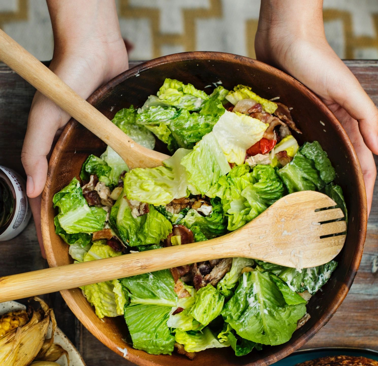 A person holding wooden spoons over a bowl of salad.