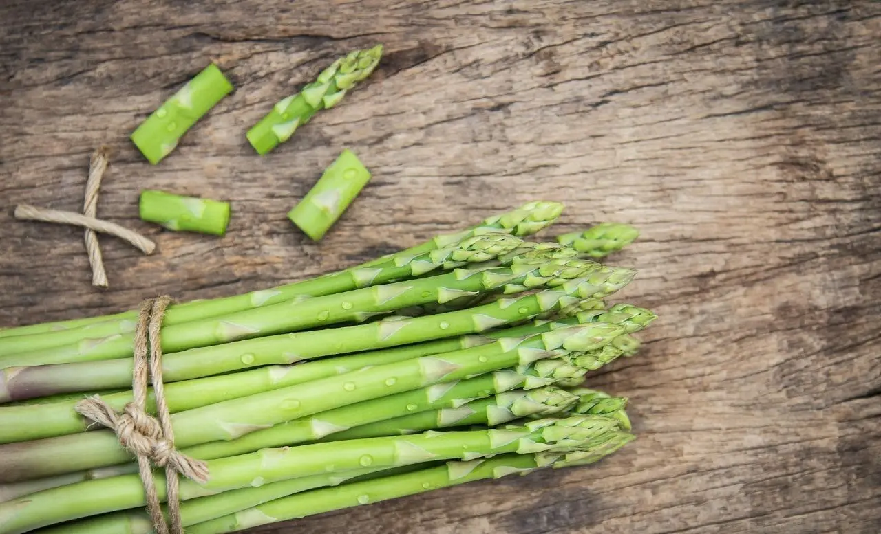 A bunch of asparagus on top of a wooden table.