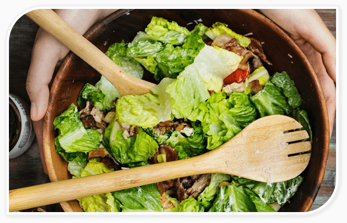 A bowl of salad with wooden spoons on the side.