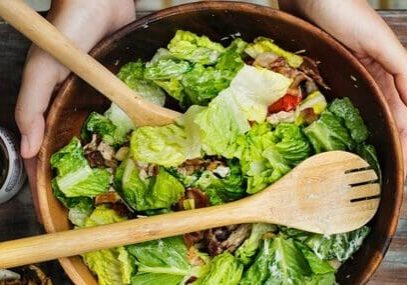 A bowl of salad with wooden spoons in it.