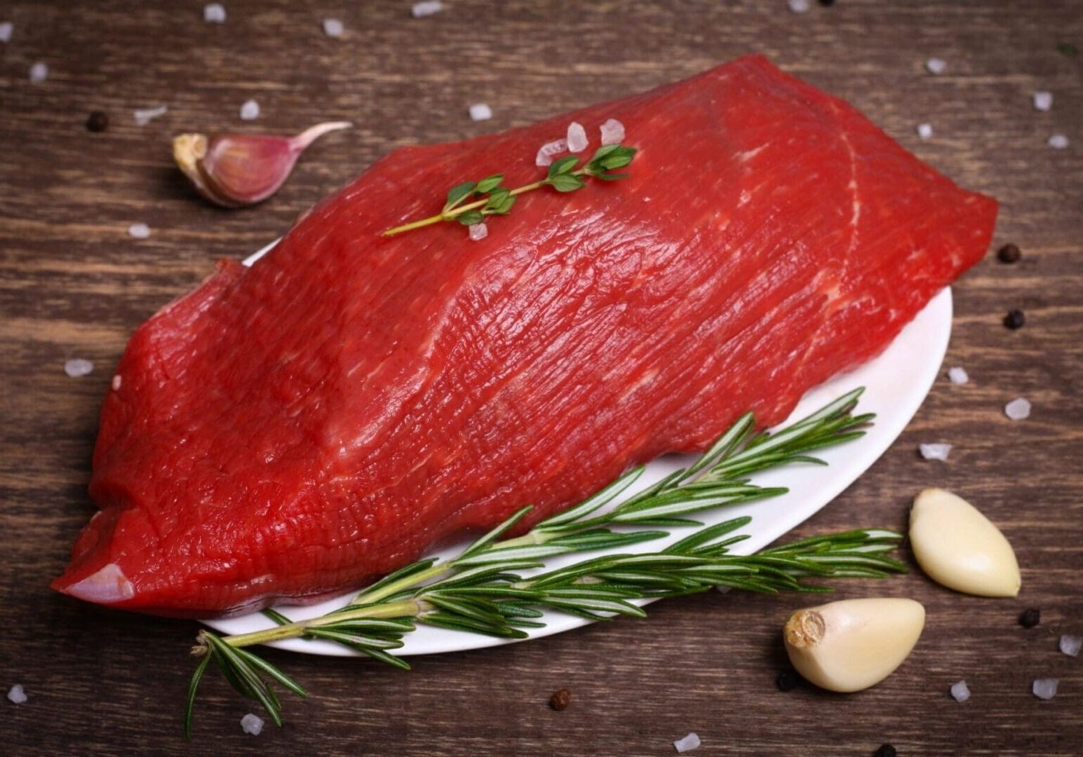 A piece of meat on a plate with garlic and rosemary.